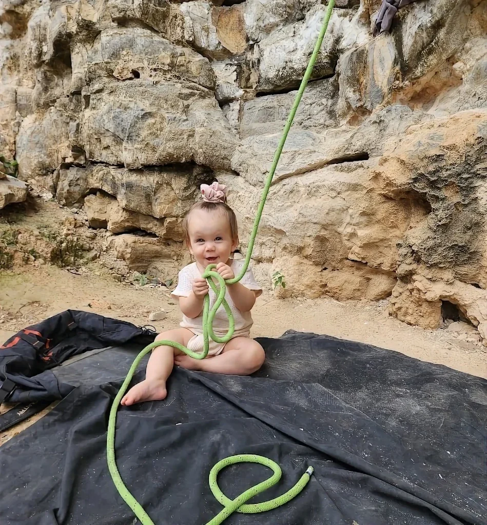 a baby at the bottom of a cliff rock climbing holding the rope