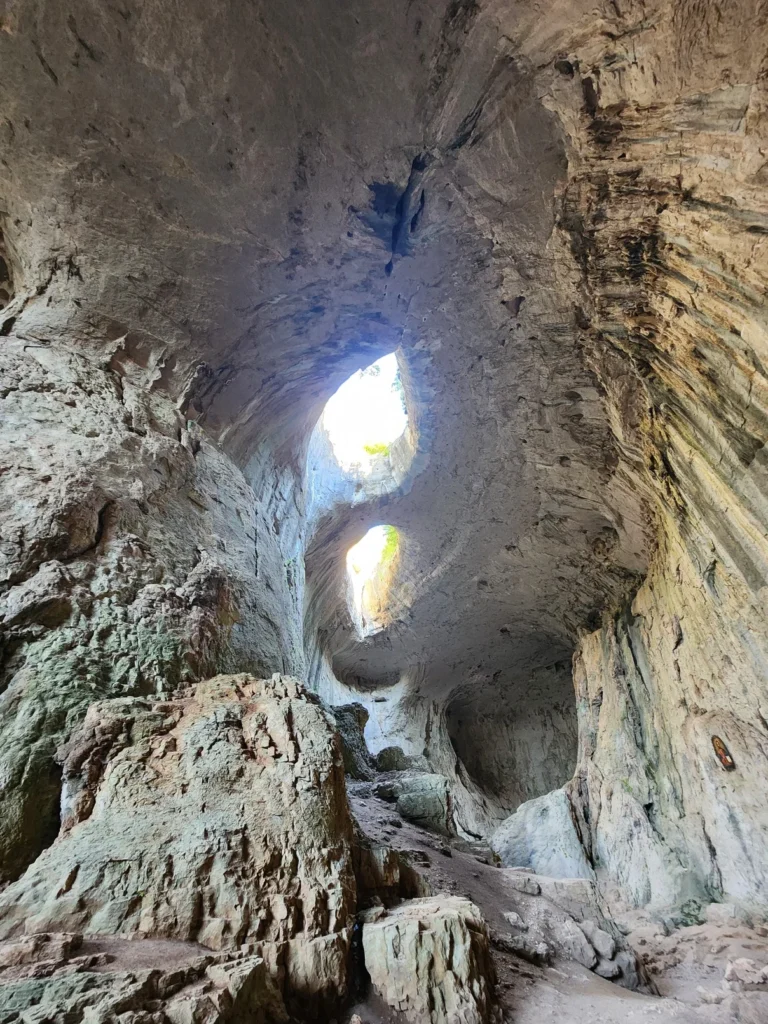 A family walking through Prohodna Cave, highlighting the vast interior and “God’s Eyes” overhead