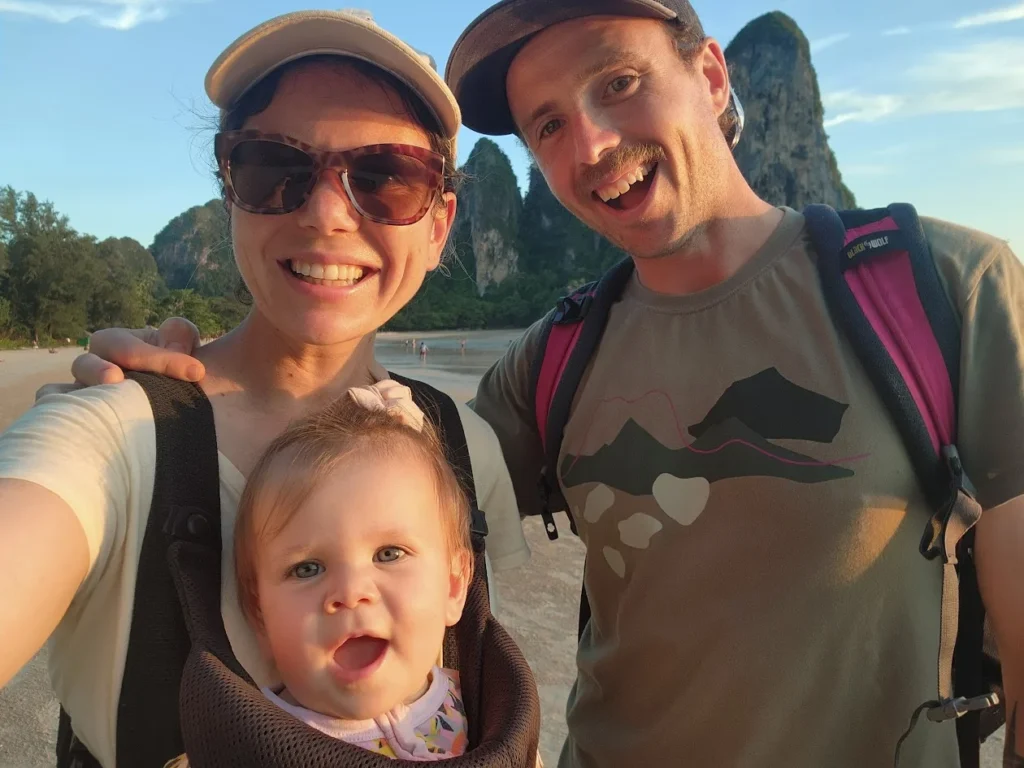 mum and dad smiling on the beach in thailand holding their baby traveling