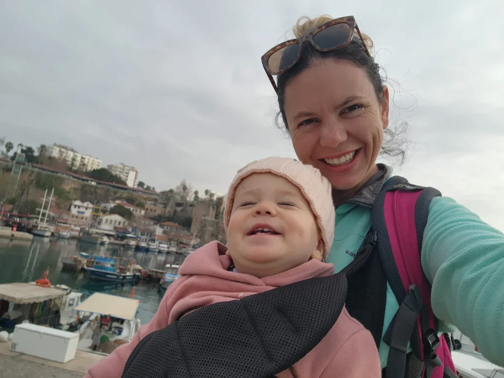 A mum holding her baby on the coast of Antalya on a pier. They are both smiling.