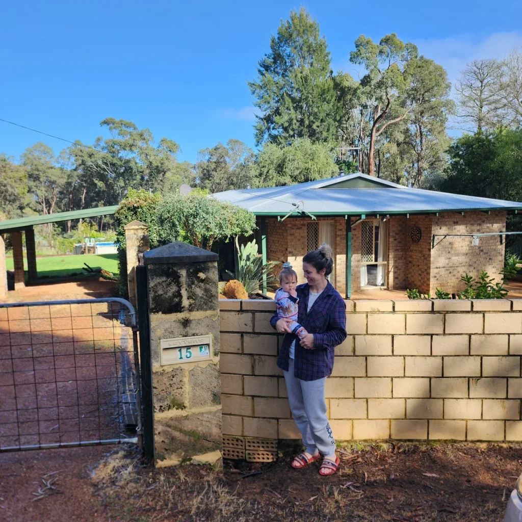 A mum and her baby standing in front of their house for the last time, smiling and emotional.