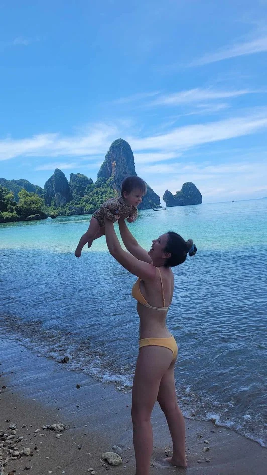 mum holding her baby in the air smiling on a beach in thailand